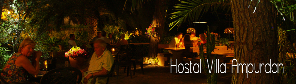 Guests at lantern-lit tables in the garden under palms and an old tree after dark